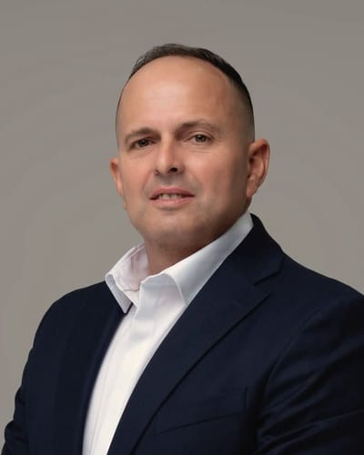 Portrait of Ariel Gomez in a navy suit and open white shirt